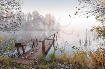Small wooden pier on still lake in autumn foggy morning