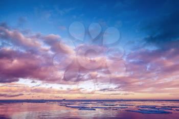 Winter coastal landscape with floating ice on sea water with colorful cloudy sky reflections. Gulf of Finland, Russia