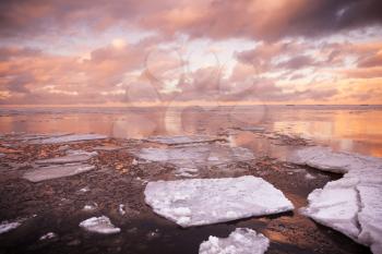 Winter coastal landscape with floating ice fragments on still sea water with red cloudy sky reflections. Gulf of Finland, Russia