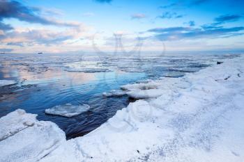 Winter coastal landscape with floating ice fragments on still water. Gulf of Finland, Russia