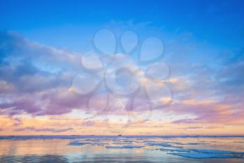 Winter coastal landscape with ice fragments and colorful cloudy sky over horizon. Gulf of Finland, Russia