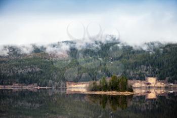 Rural Norwegian landscape with still lake water and clouds over mountains 