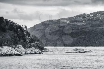 Spring Norwegian coastal landscape with sea and dark mountains. Monochrome photo