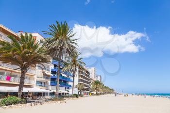 Modern buildings and palms on coastal street of Calafell resort town in sunny summer day. Tarragona region, Catalonia, Spain
