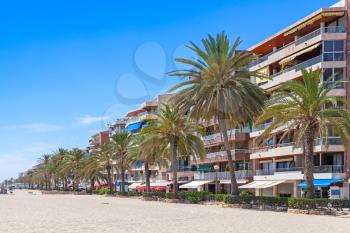 Modern buildings and palm trees on coastal street of Calafell resort town in sunny summer day. Tarragona region, Catalonia, Spain