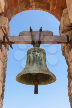Old bell hanging in stone arch, ancient fortress of Calafell town, Spain