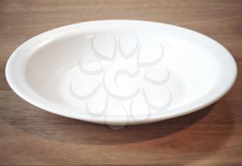 Empty white plate at angle on the wooden table