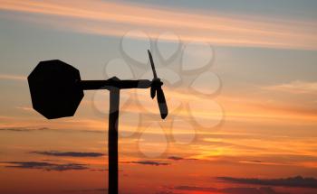 Small windmill style weather vane silhouette above orange sunset sky