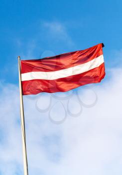 Flag of Latvia above blue sky with clouds