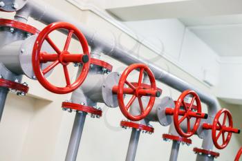 Red industrial valves in a row on gray pipelines system