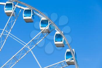 Ferris wheel with white cabins on blue sky background