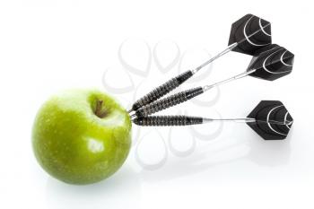 Green apple as a target for black steel darts, closeup photo on white background