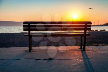 Outdoor empty bench on a sea coast with shining morning sun on a background, vintage toned photo, with lens flare effect 