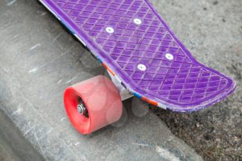 Modern skateboard stands on the curb of asphalt road, close-up fragment