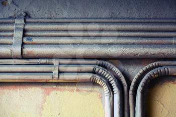 Abstract industrial background, group of bent vintage electrical conduits mounted on a concrete wall.  Old style toned, photo filter effect