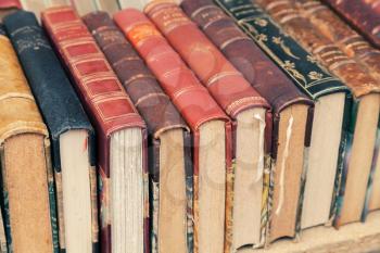 Old used vintage books with colorful leather covers lay on the shelf