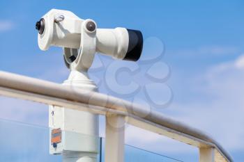 White stationary paid telescope stands on sea coast over blue sky background
