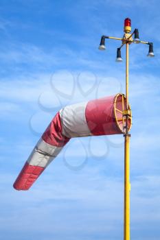 Windsock as an airport equipment. Red and white striped wind indicator over blue cloudy sky