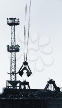 Cargo port fragment with industrial constructions and grapple loader on ropes, vertical monochrome photo