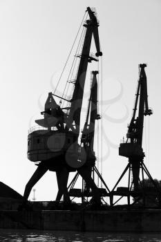 Dark silhouettes of industrial port cranes. Danube River coast, Bulgaria. Black and white vertical photo