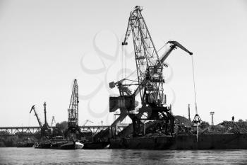 Dark silhouettes of industrial port cranes on Danube River, Bulgaria. Black and white photo