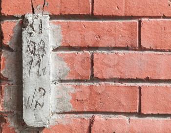 Special concrete block with installation date for observing cracks in red brick wall