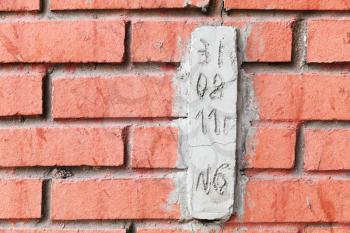 Special concrete block with date for observing cracks in red brick wall