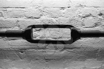 Old black turnbuckle, close-up photo over white brick wall background