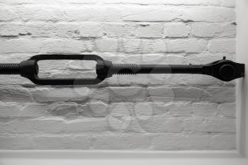 Old black turnbuckle used in building structure over white brick wall background