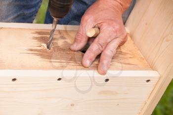 Homemade birdhouse made of wood under construction, carpenter works with drill, close-up photo