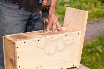 Wooden birdhouse is under construction, carpenter works with drill, closeup photo