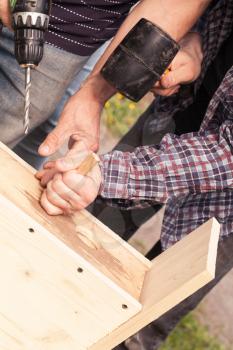 Wooden birdhouse is under construction, carpenters work with rubber hummer and drill