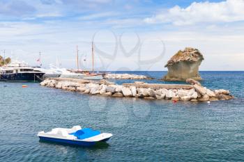 Coastal seascape of Lacco Ameno, Ischia island, Italy. Small white catamaran and Il Fungo, mushroom shaped rock on a background
