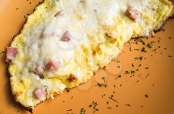 Freshly roasted omelet with ham and cheese on orange plate. Breakfast theme