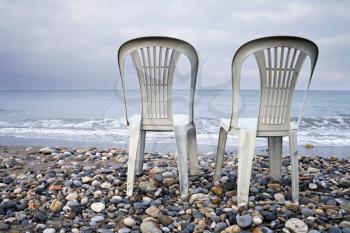 Two empty plastic chairs on the coast of Mediterranean Sea. Overcast Season