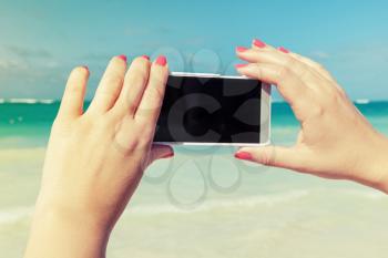 Woman using smart phone for taking outdoor photo on a beach in Dominican republic. Vintage style, filter effect