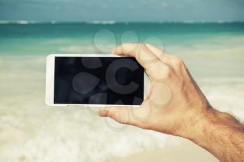 Man using smart phone for taking photo on a beach in Dominican republic. Vintage style, filter effect