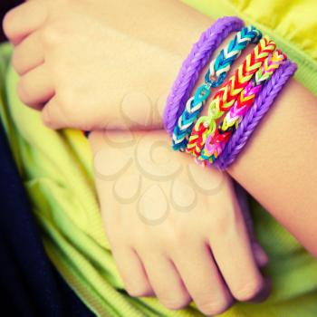 Child hands with Colorful rubber rainbow loom band bracelets, trendy kids fashion accessories.  Vintage retro tonal photo filter correction
