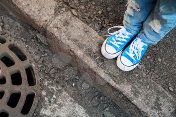 Teenager feet in jeans and blue shoes stand on the street edge. Photo with selective focus and shallow DOF