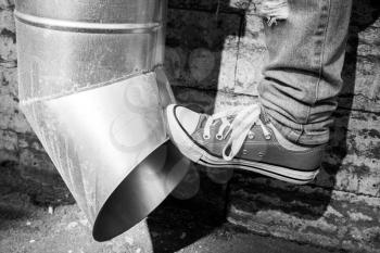 Teenager in sneakers kicks drainpipe, black and white urban photo 