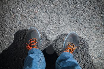 Male feet in sport shoes standing on asphalt road pavement