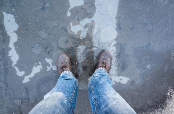 Male feet standing on frozen puddle with thin ice and falling leaves