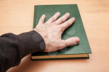 Male hand laying on book with empty dark green leather cover