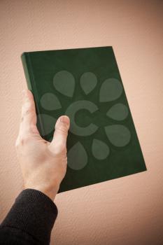 Book with empty dark green leather cover in male hand, vignette photo filter effect