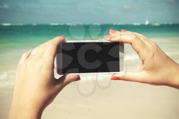 Woman holds smart phone in hands for taking outdoor photo on a summer beach in Dominican republic. Vintage tonal correction photo filter, old style effect