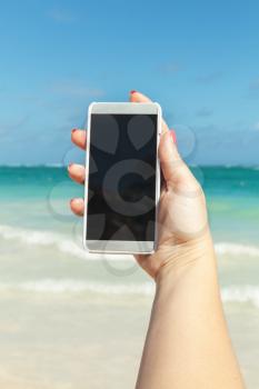 Woman holds smart phone in hand for taking photo on a beach in Dominican republic