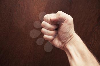Strong male fist over dark brown wooden background
