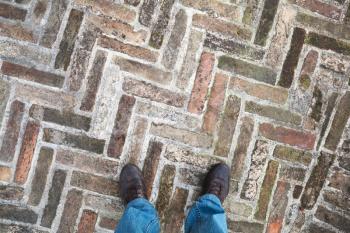Male feet in new black shining leather shoes stand on old cobblestone pavement, first person view