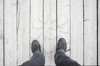 Male feet in leather shoes stand on white wooden floor, first person view
