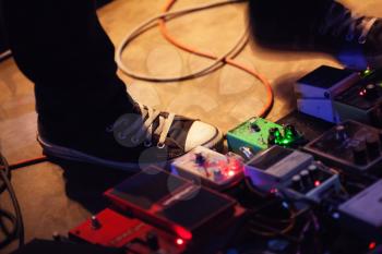 Feet of guitar player on a stage with set of distortion effect pedals. Selective focus
